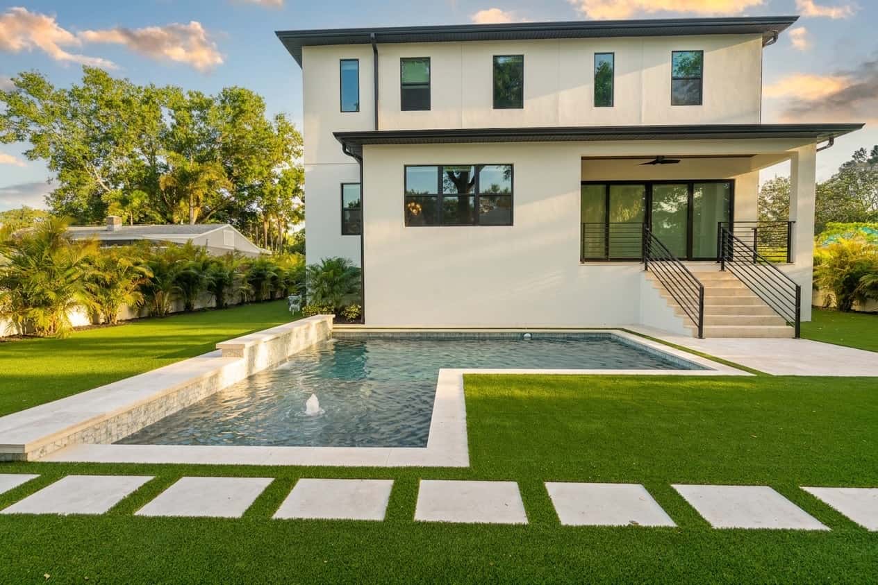 Custom pool, turf lawn, and paver stepping stones by LIV Pools at a modern Largo, FL home at golden hour