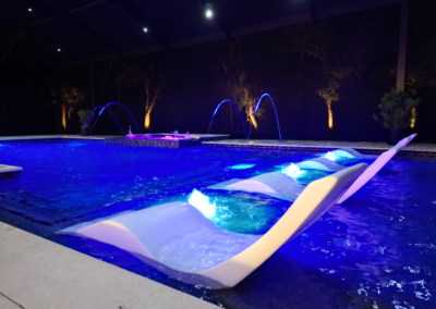 A pool at night with ledge loungers and bubblers